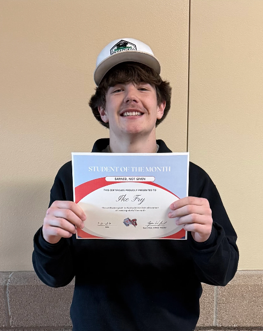 A smiling young man in a baseball cap holds a "Student of the Month" certificate.