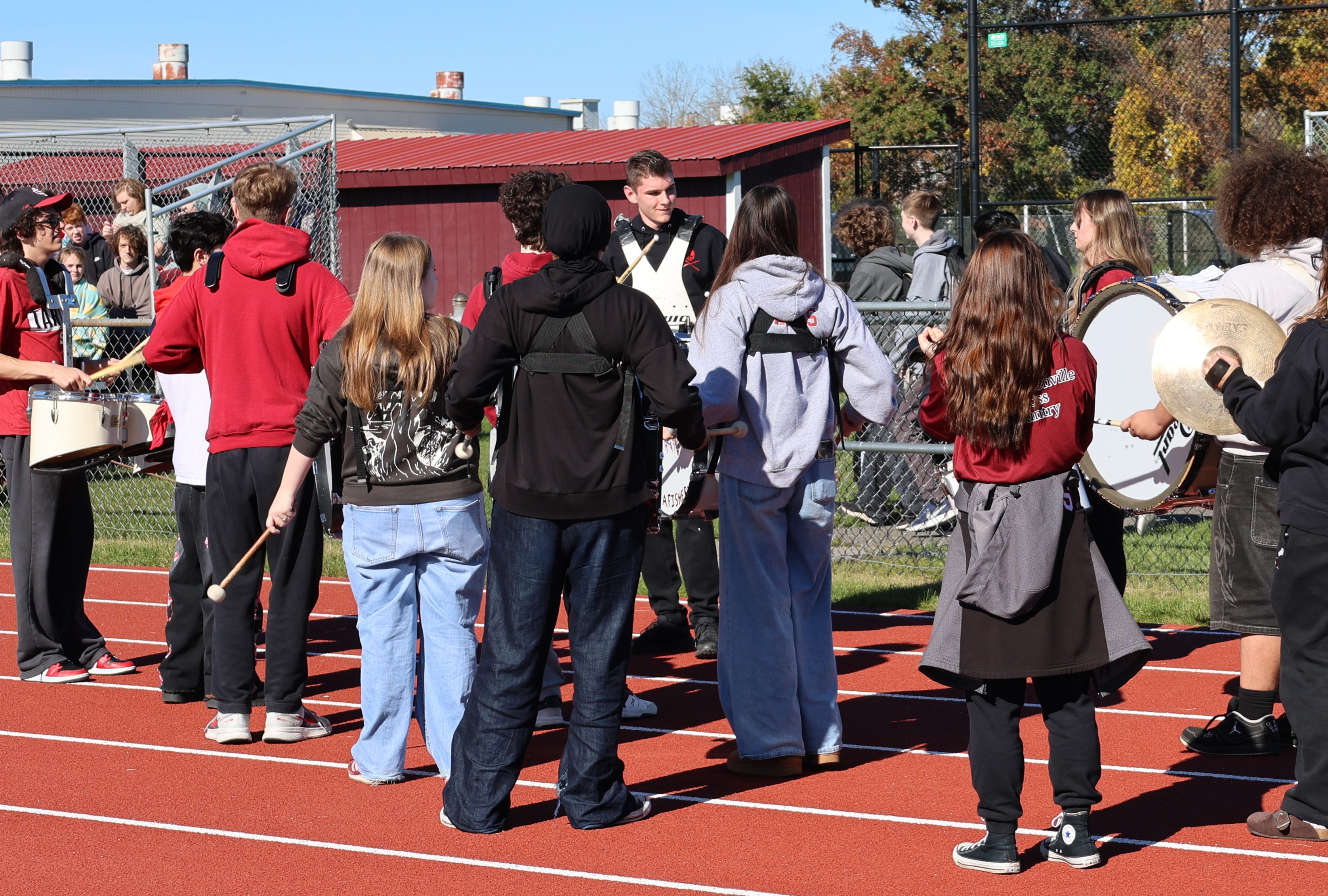 A marching band practicing outdoors on a red running track on a sunny day.