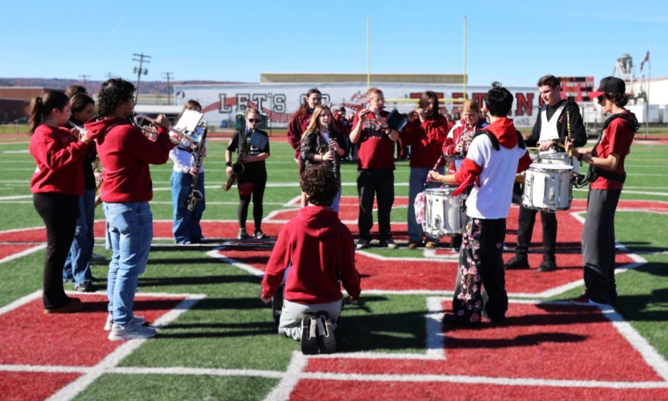 A high school marching band rehearses on a sunny outdoor football field, practicing their instruments and formations.