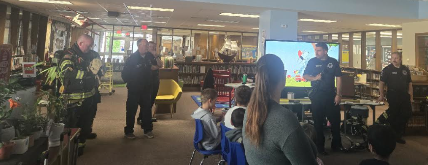 Firefighters visit a school library to speak with a group of students.