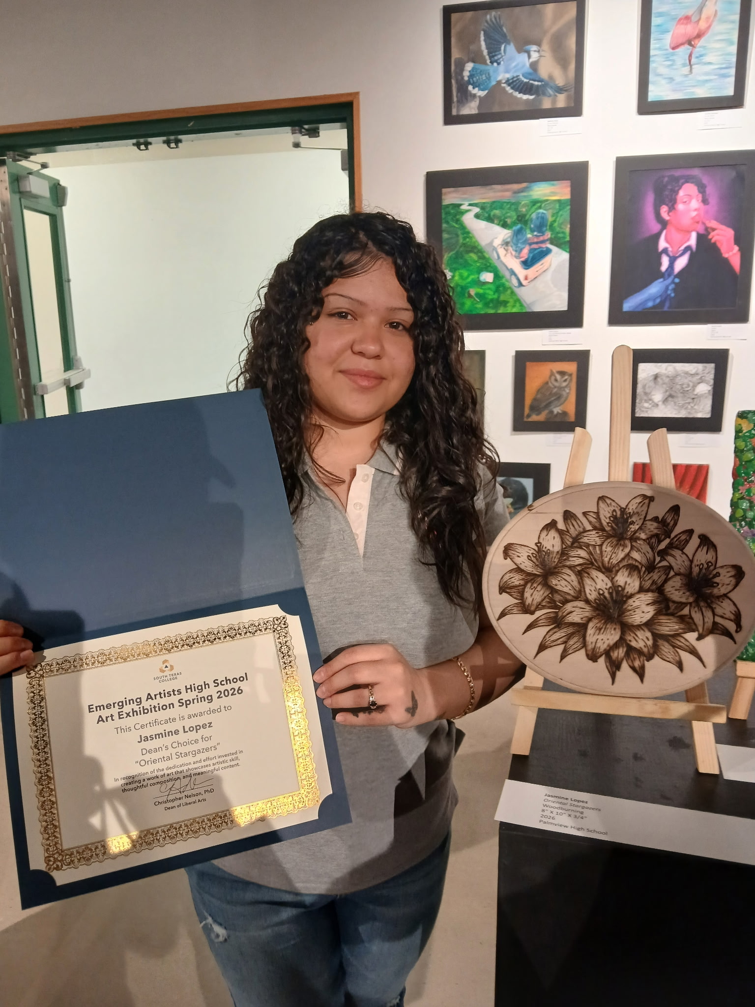 Jasmine Lopez proudly holds a certificate and a woodburned art piece featuring lilies.