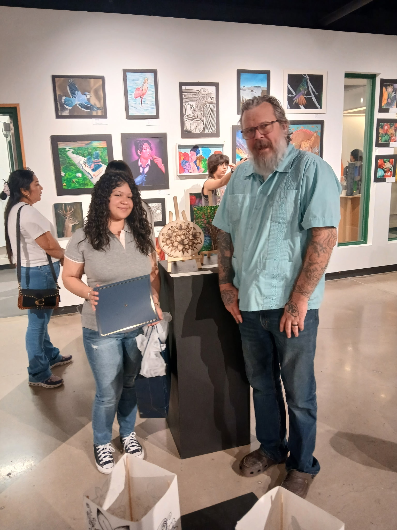 Jasmine Lopez holds a blue folder in front of a wall of framed artwork.