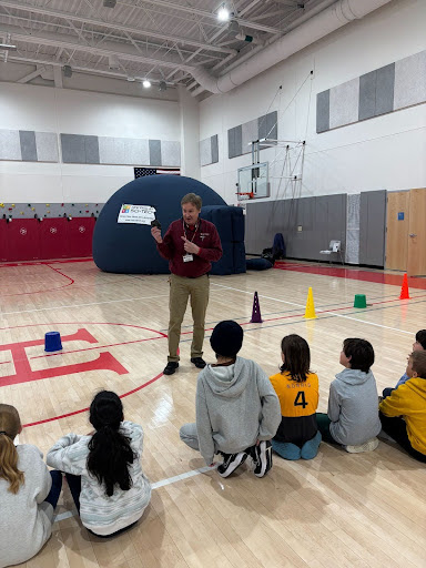 Students engaging in a planetarium presentation as part of Creative Arts and Sciences (CAS). An instructor stands in front of them with a planet demonstration in the background.