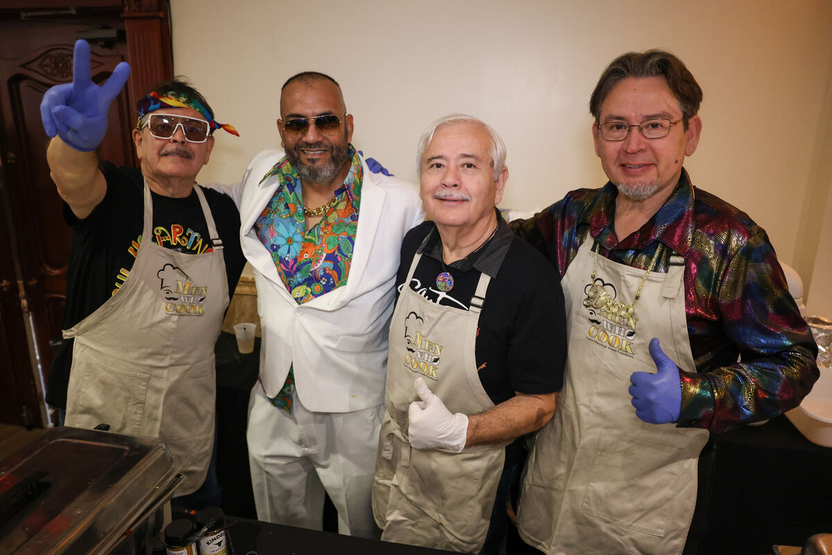Four men in aprons and colorful attire pose for a photo, with one giving a peace sign.