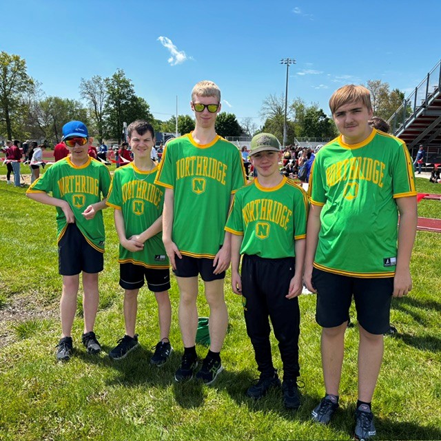 Five young athletes in green 'Northridge' shirts stand on a grassy field under a blue sky.