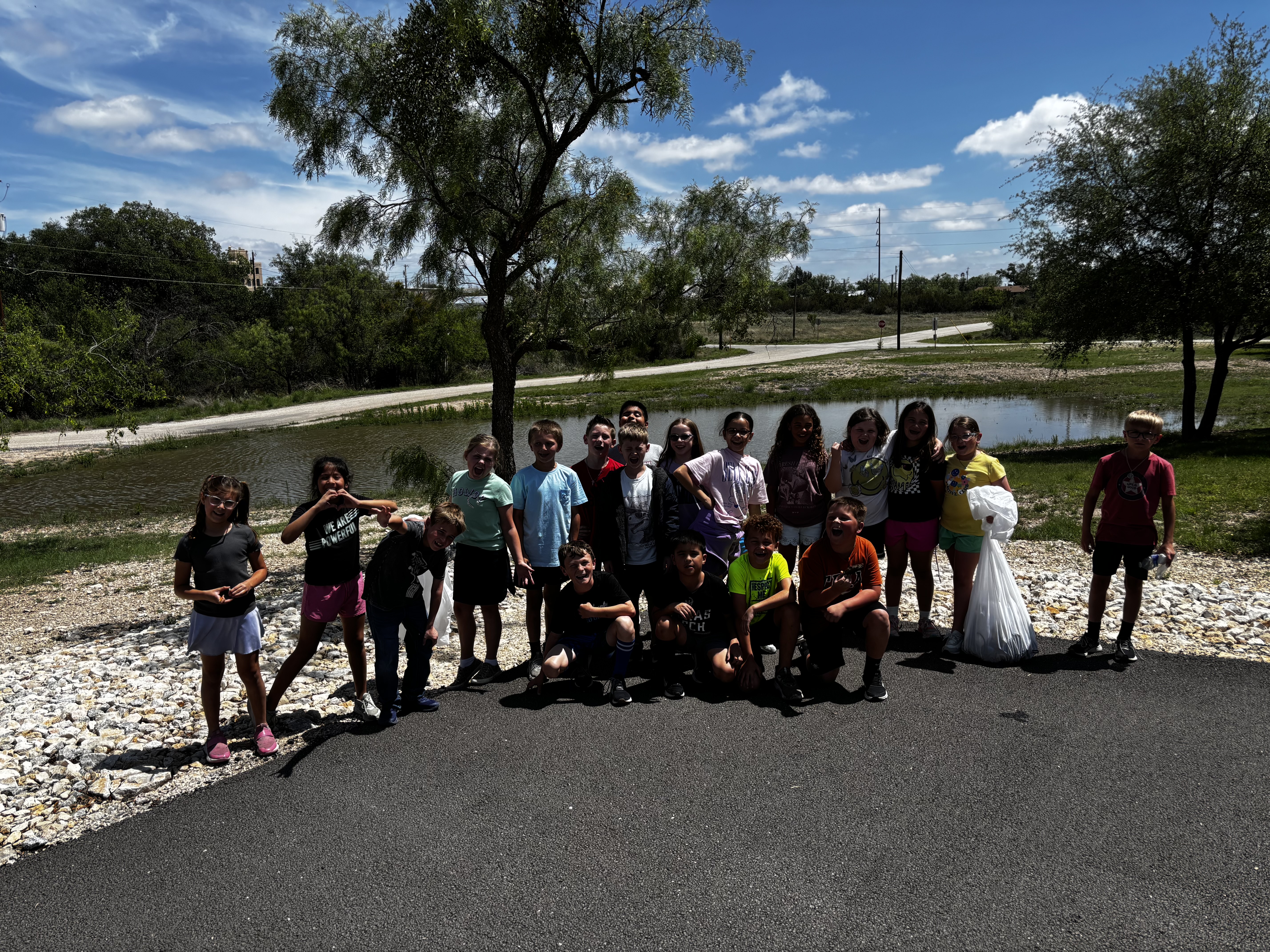 A diverse group of children stand together outdoors near a body of water, smiling and posing for a photo.