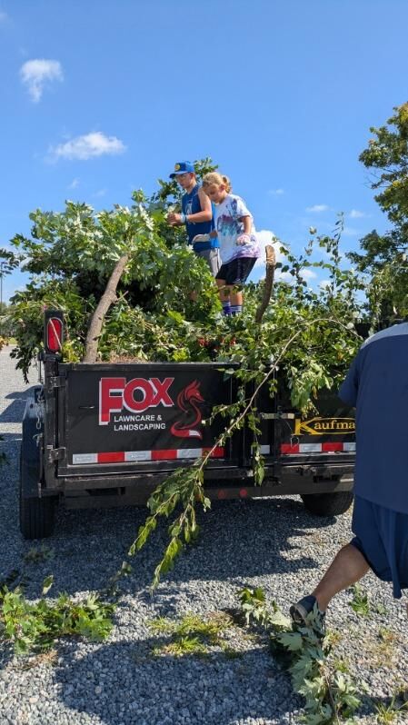 People standing in the back of a trailer with a pile of cut tree limbs