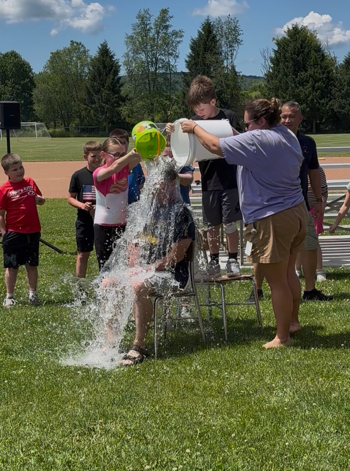 Children pour water from buckets onto a person sitting on a chair outdoors.