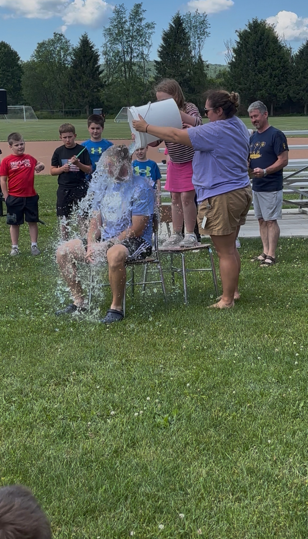 A person sits on a chair as a bucket of water is poured over their head, creating a large splash.