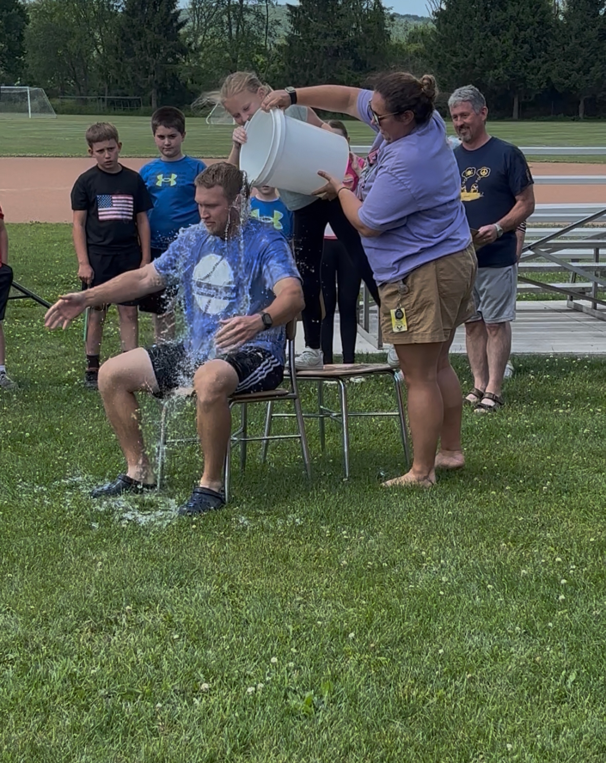 A man is doused with water from a bucket by a woman, while children watch.
