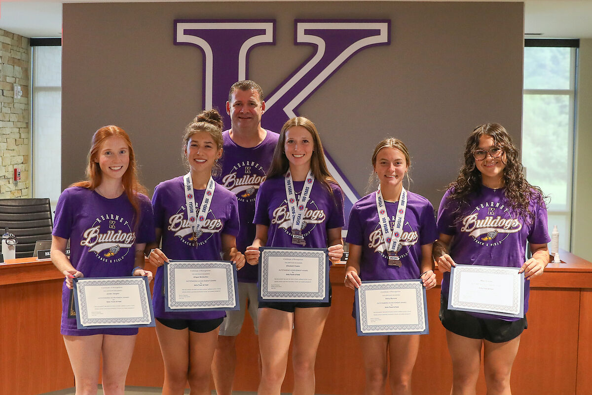 Five young women in purple 'Kearney Bulldogs Track & Field' shirts proudly hold certificates and medals.