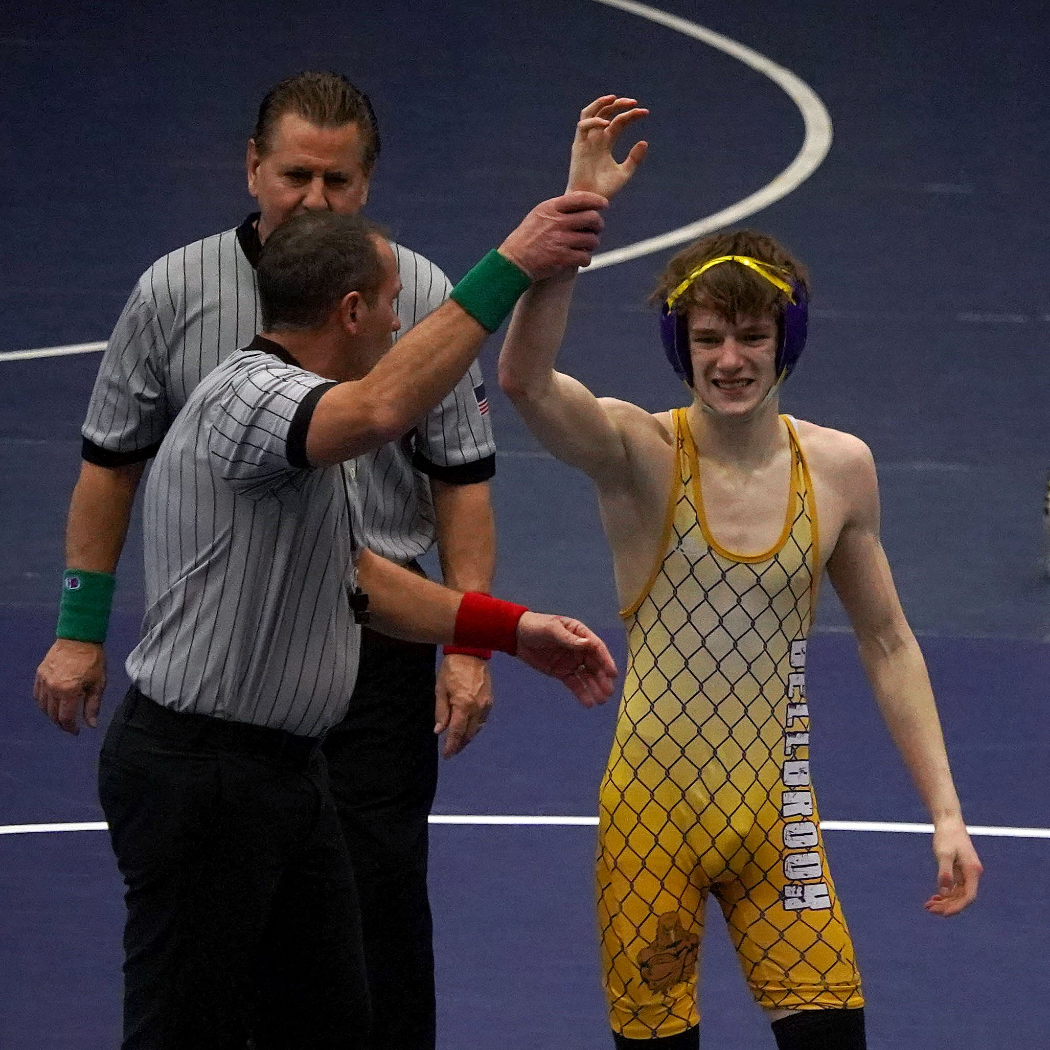A wrestler's arm is raised after a win by two referees