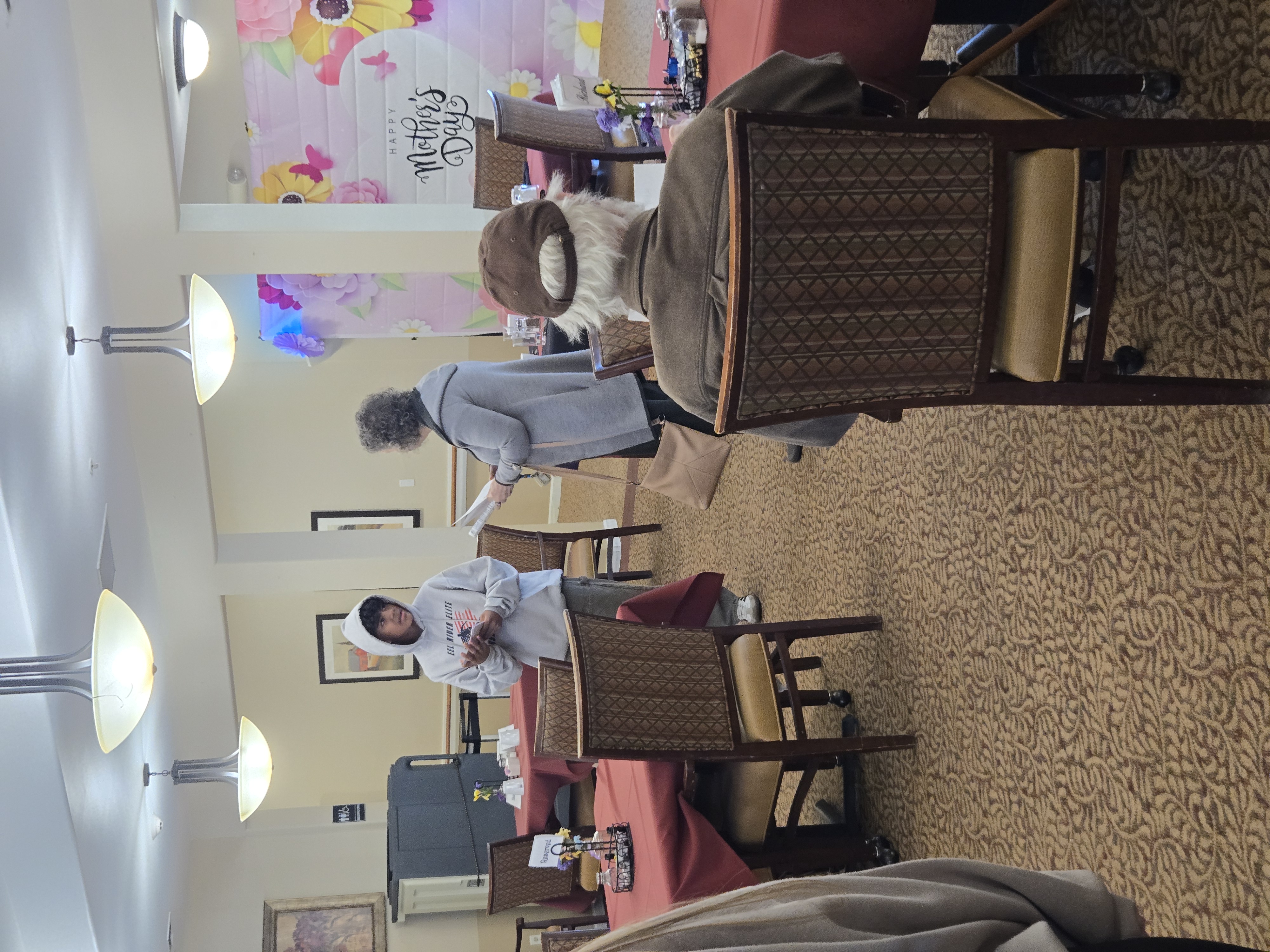 A 'Happy Mother's Day' banner with floral decorations hangs in a room with tables and chairs.