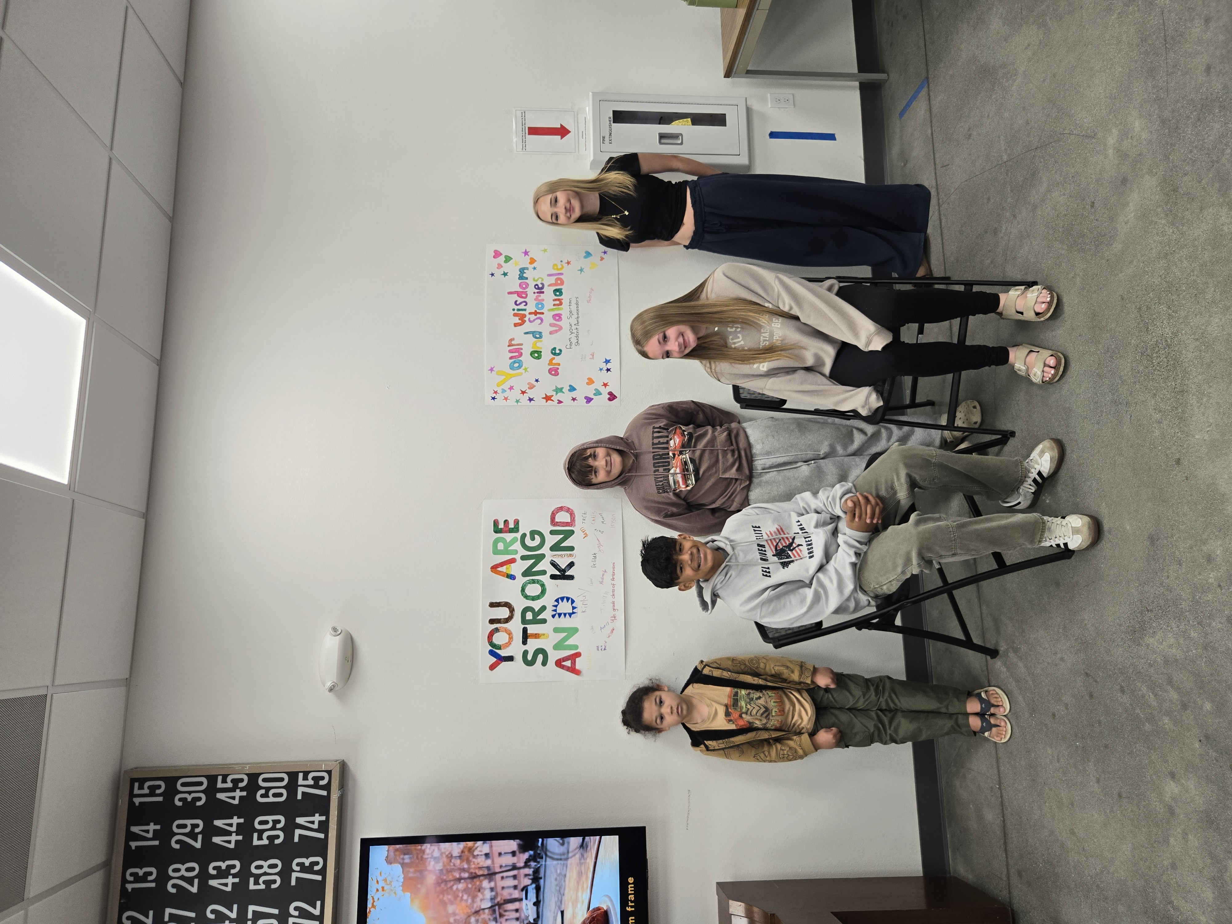 Six students sit in chairs in front of a wall with motivational posters.