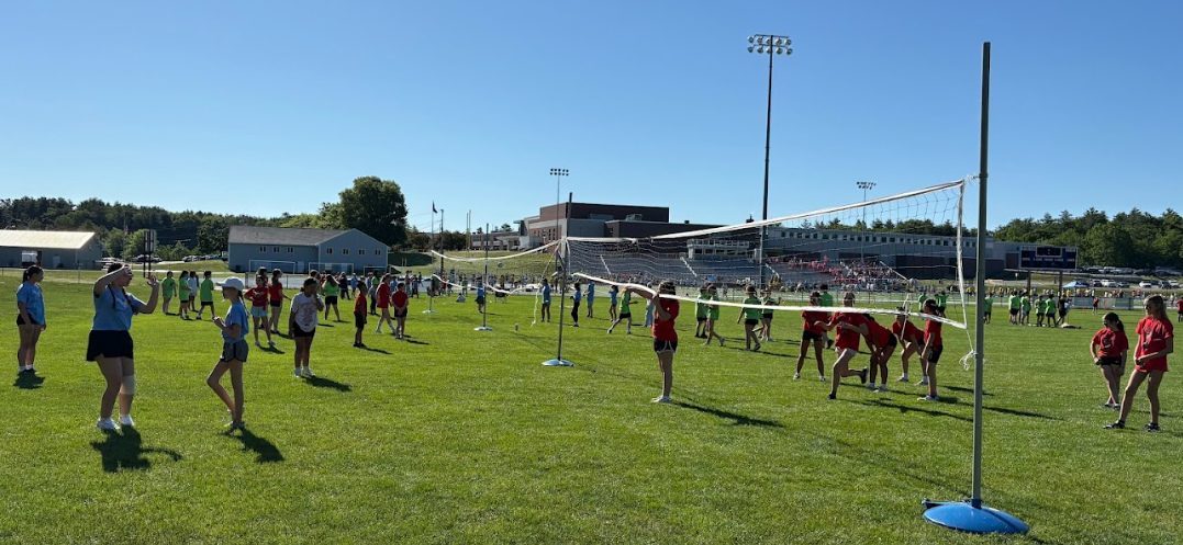 Young athletes practice volleyball on a sunny day on a grassy field with multiple nets.