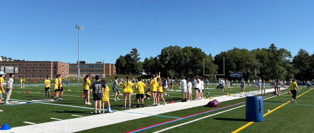 A group of students in yellow shirts participate in an outdoor activity on a sports field.