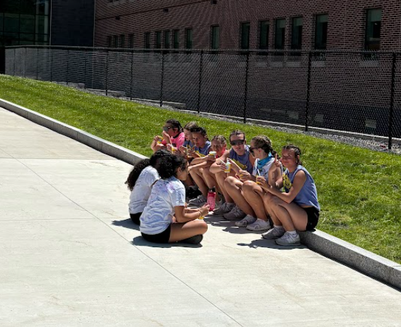 A group of young people sit together outdoors, some holding yellow cups.