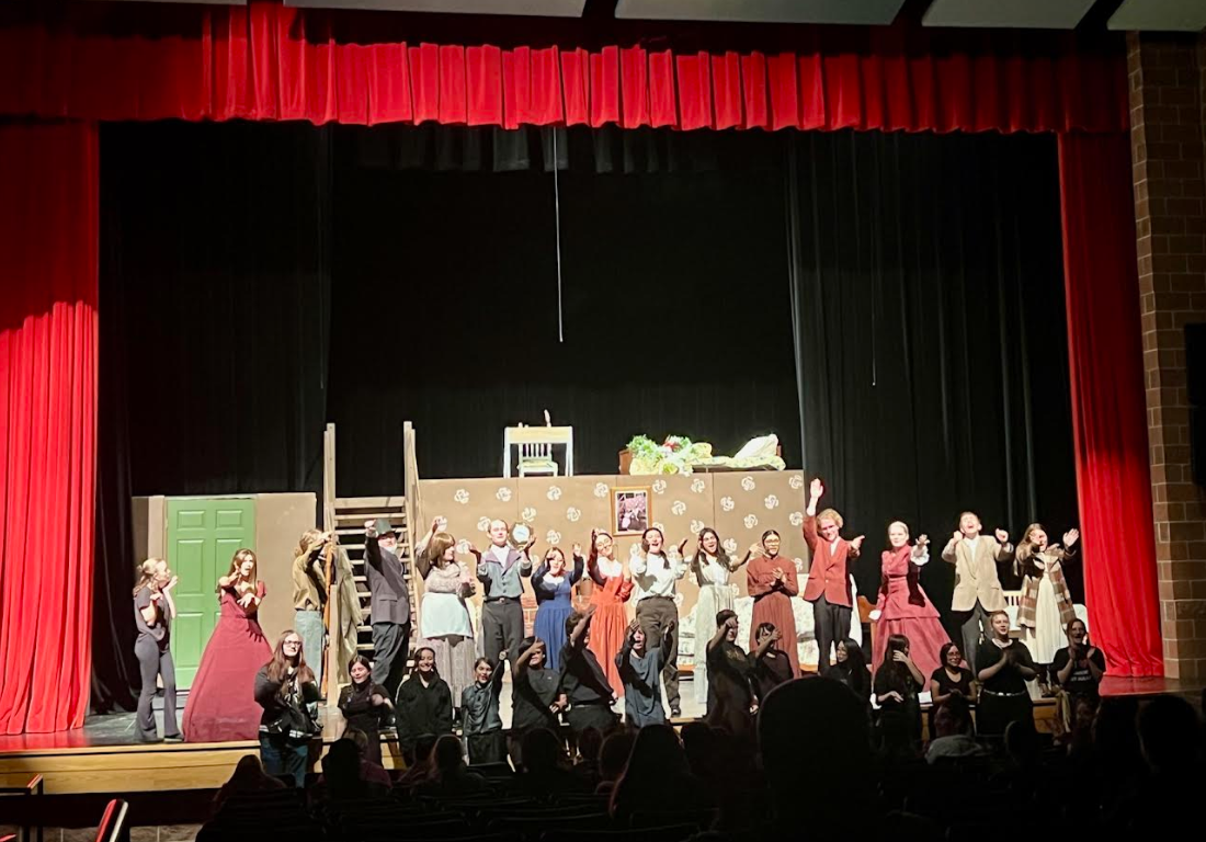 A cast of actors in period costumes takes a bow on a theater stage.