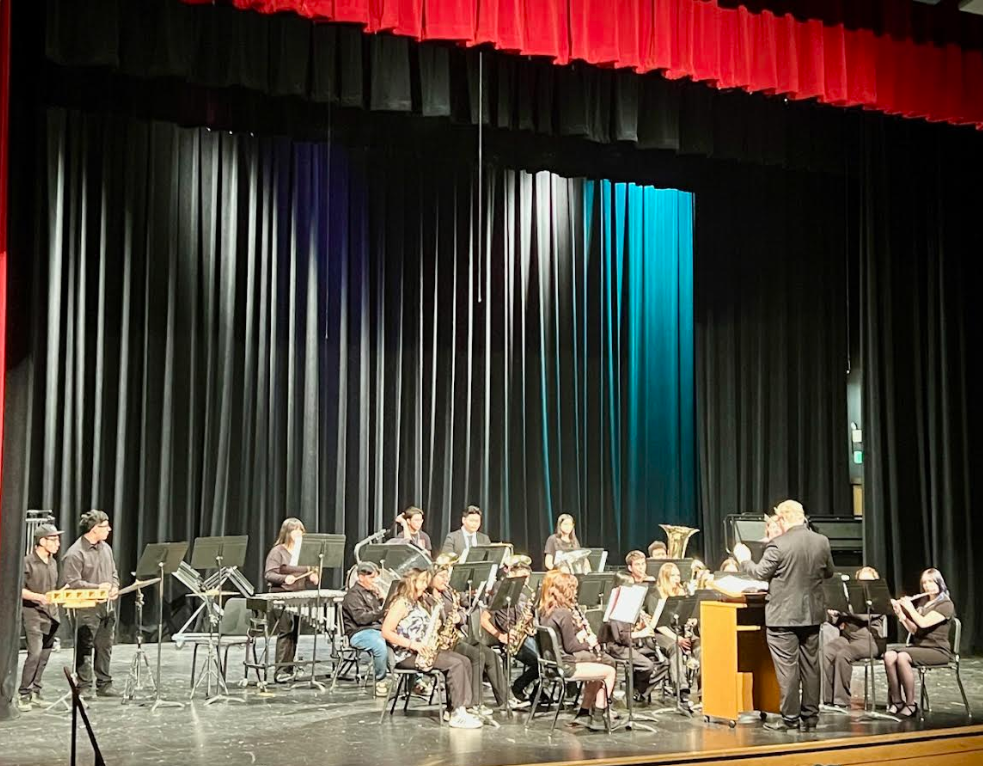 A high school band performs on stage with a conductor.