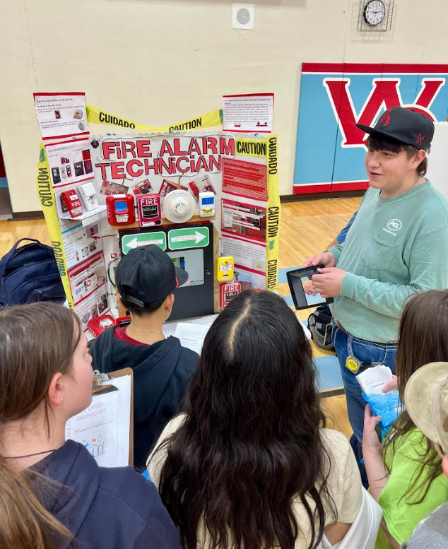 A young person presents a science fair project about fire alarm technicians, displaying various components.