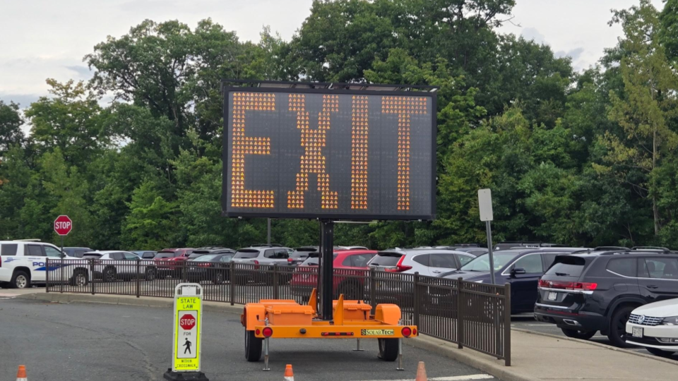 A digital message board on a trailer reads 'EXIT' in glowing orange letters in a parking lot.