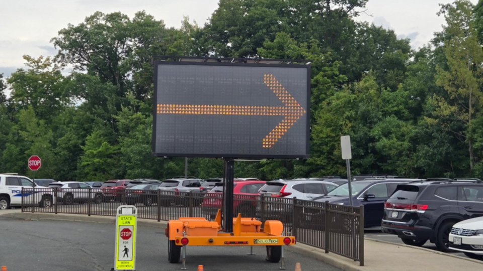 A digital traffic sign on a trailer displays a large yellow arrow pointing right in a parking lot.