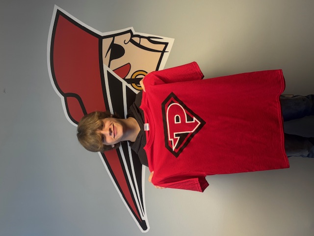 A young person smiles while holding up a red t-shirt with a stylized 'P' logo.