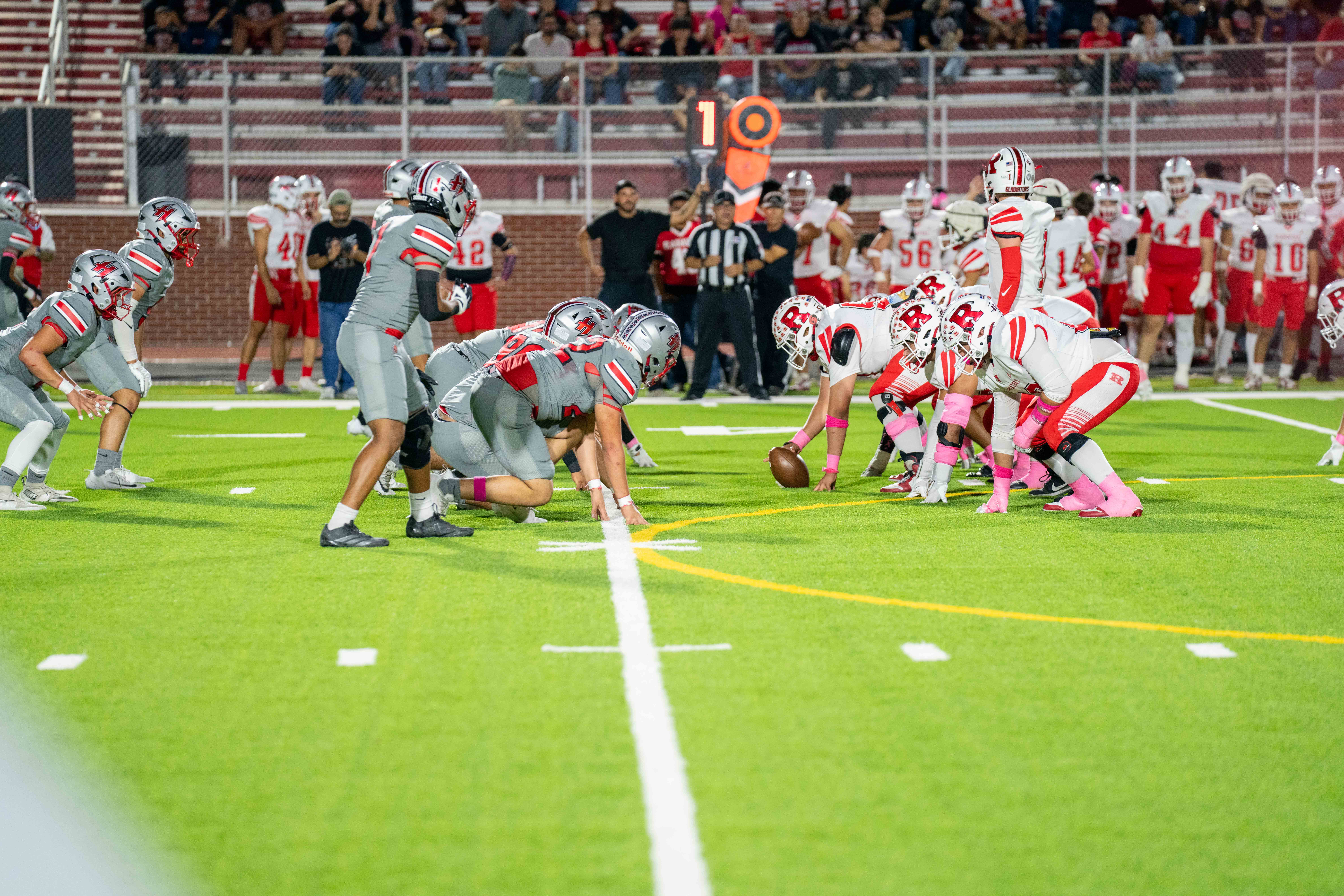 Two high school football teams line up face-to-face on a green turf field, ready for the snap.