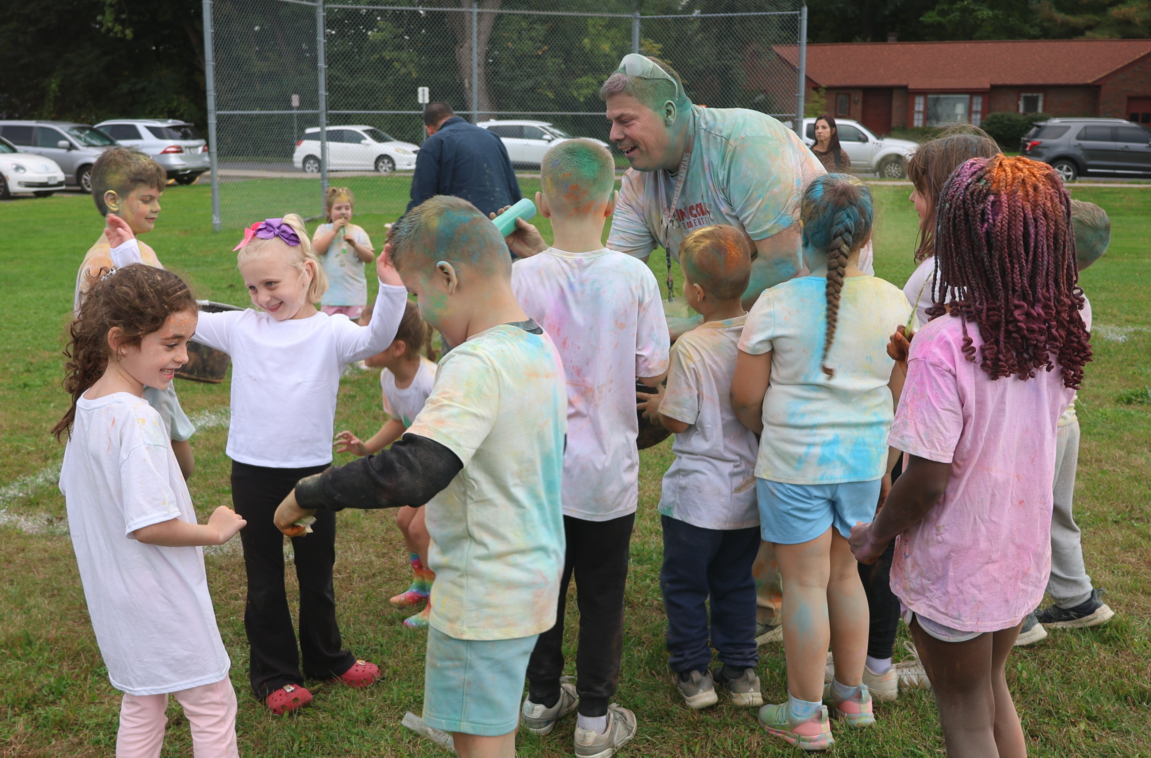 A group of children and an adult are covered in colorful powder outdoors on a grassy field.