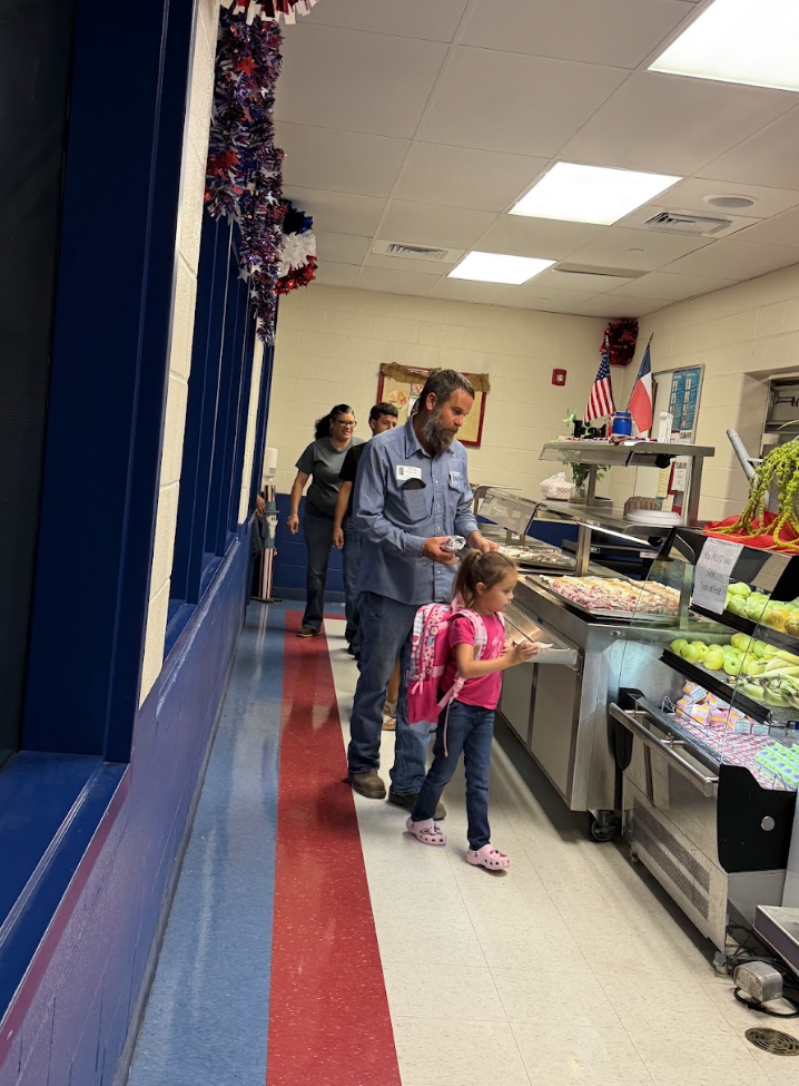 People line up in a school cafeteria to select food items from the serving stations.