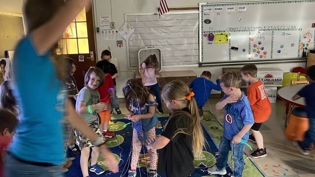 Children in a classroom are playing with glow sticks and streamers, creating a festive atmosphere.