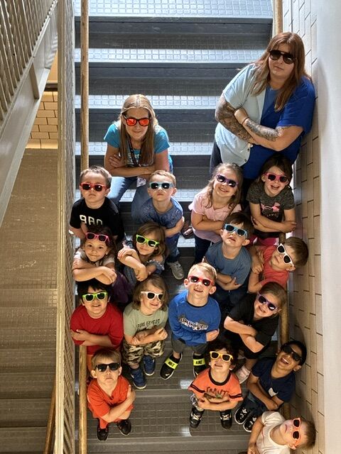 A group of children and an adult wearing sunglasses pose on stairs.