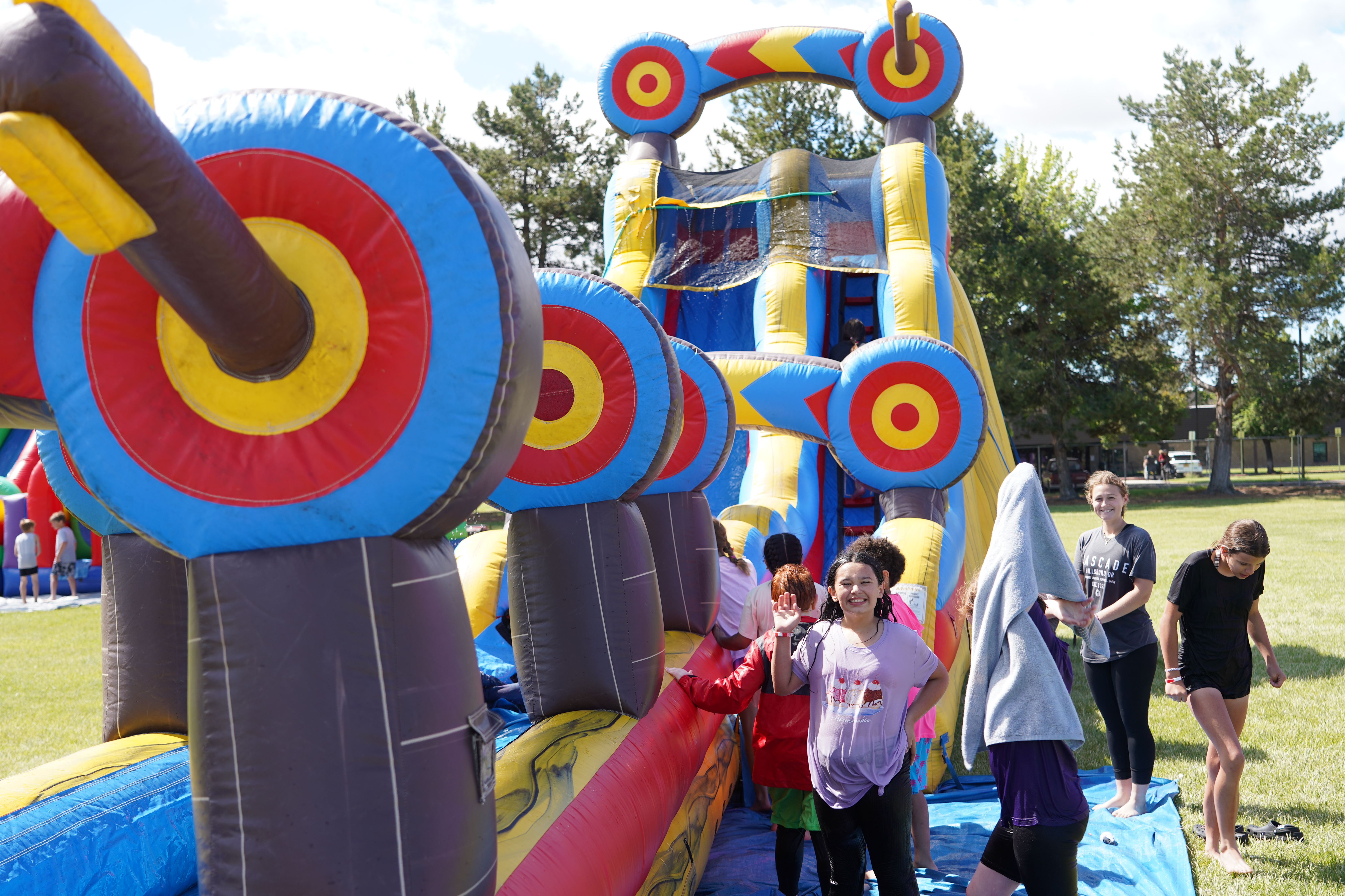 Children laugh and play on a colorful inflatable obstacle course on a sunny day.