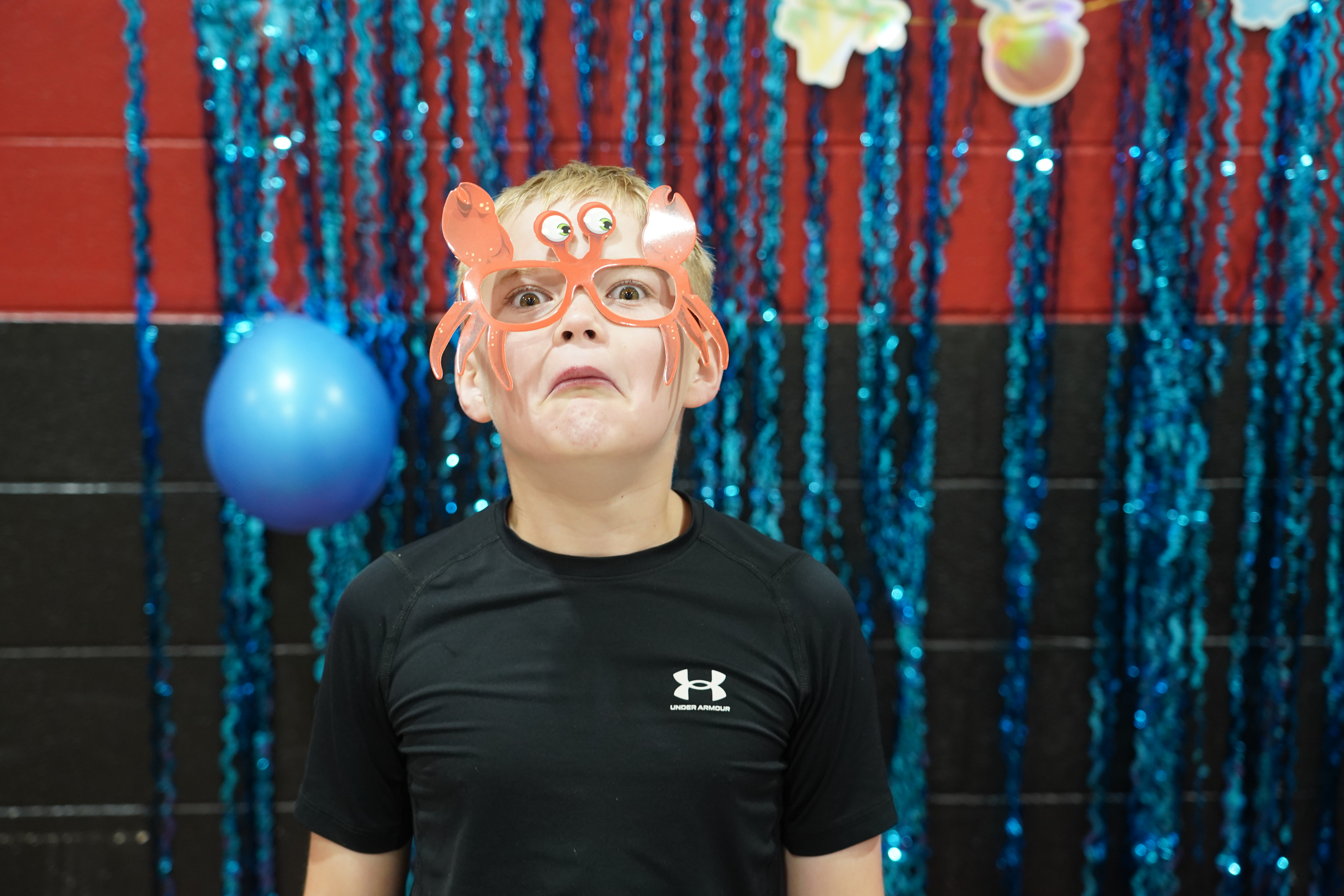 A young boy with blonde hair makes a funny face while wearing oversized orange crab glasses.