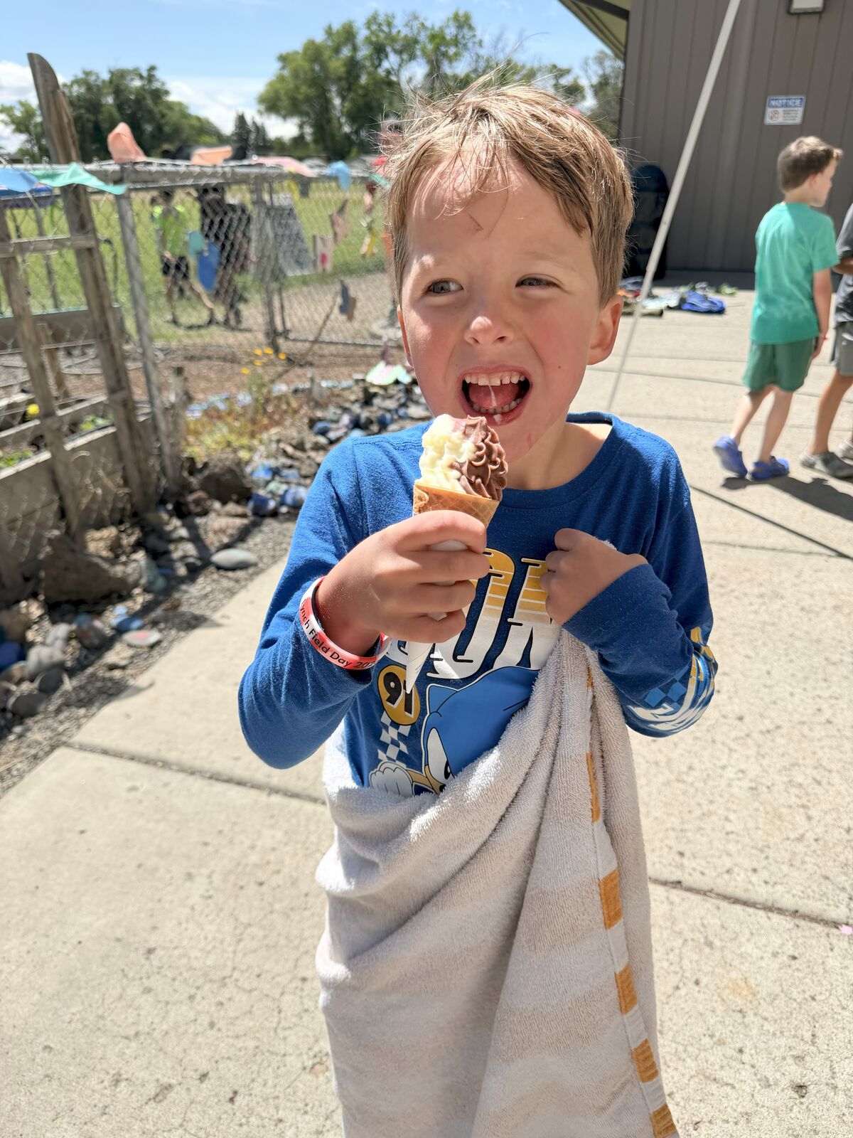 A young boy in a blue shirt enjoys a swirl ice cream cone outdoors.