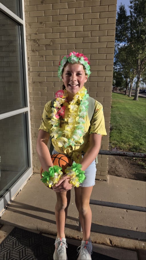 A smiling girl wearing flower leis, a headband, and wristbands holds a basketball outdoors.
