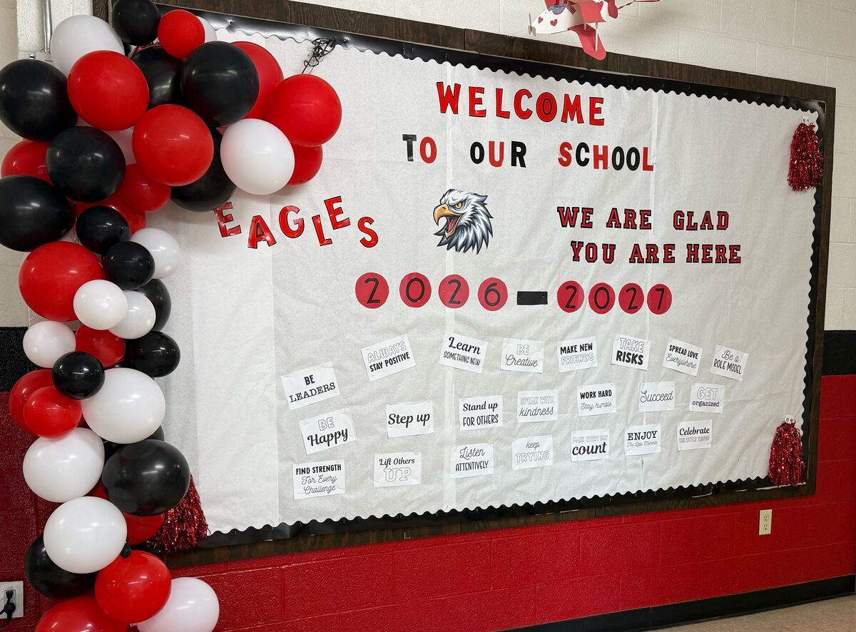 A school bulletin board decorated with red, black, and white balloons welcomes students with the message 'WELCOME TO OUR SCHOOL'.