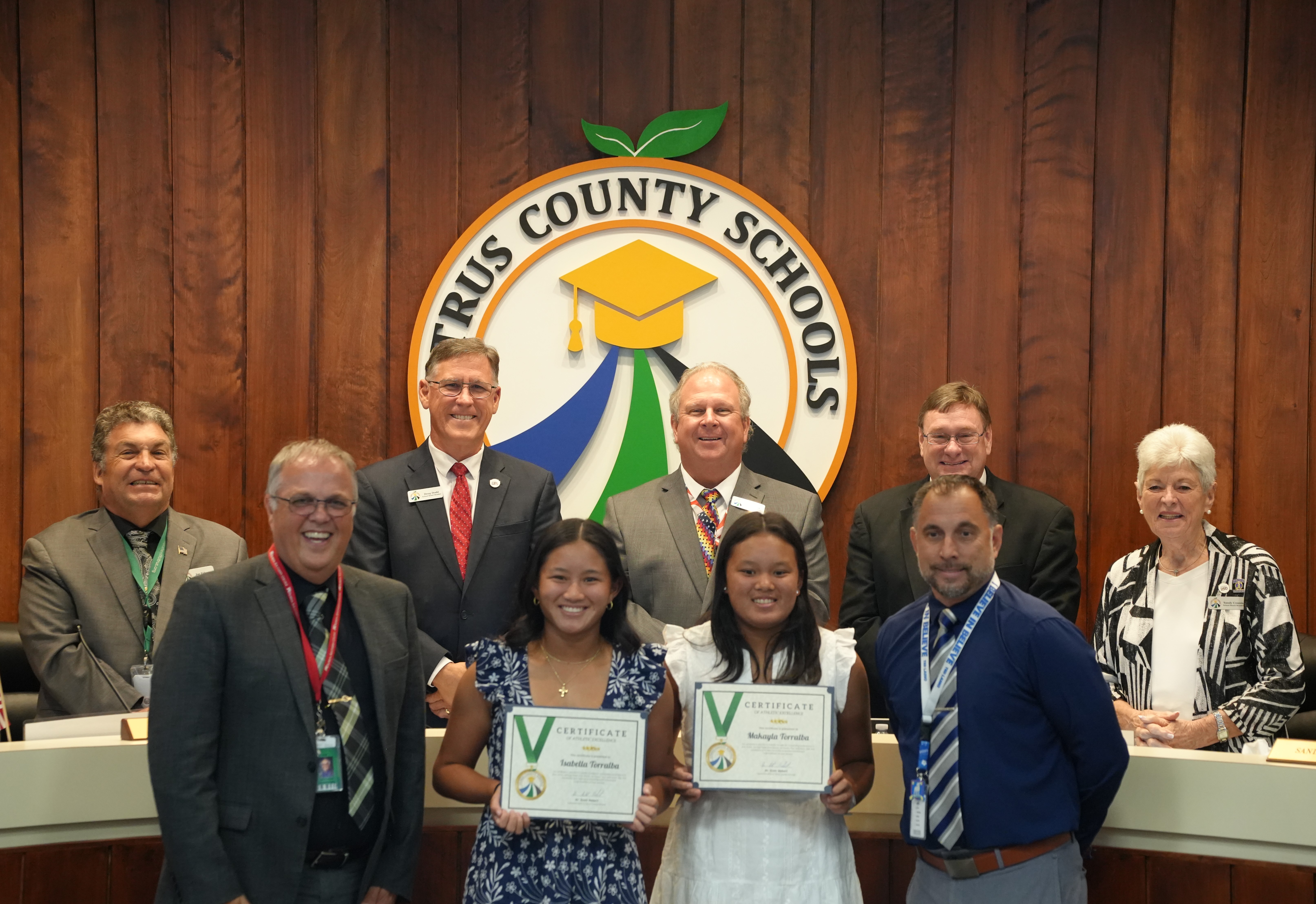 Two young women proudly hold certificates of athletic excellence in front of a Citrus County Schools logo.