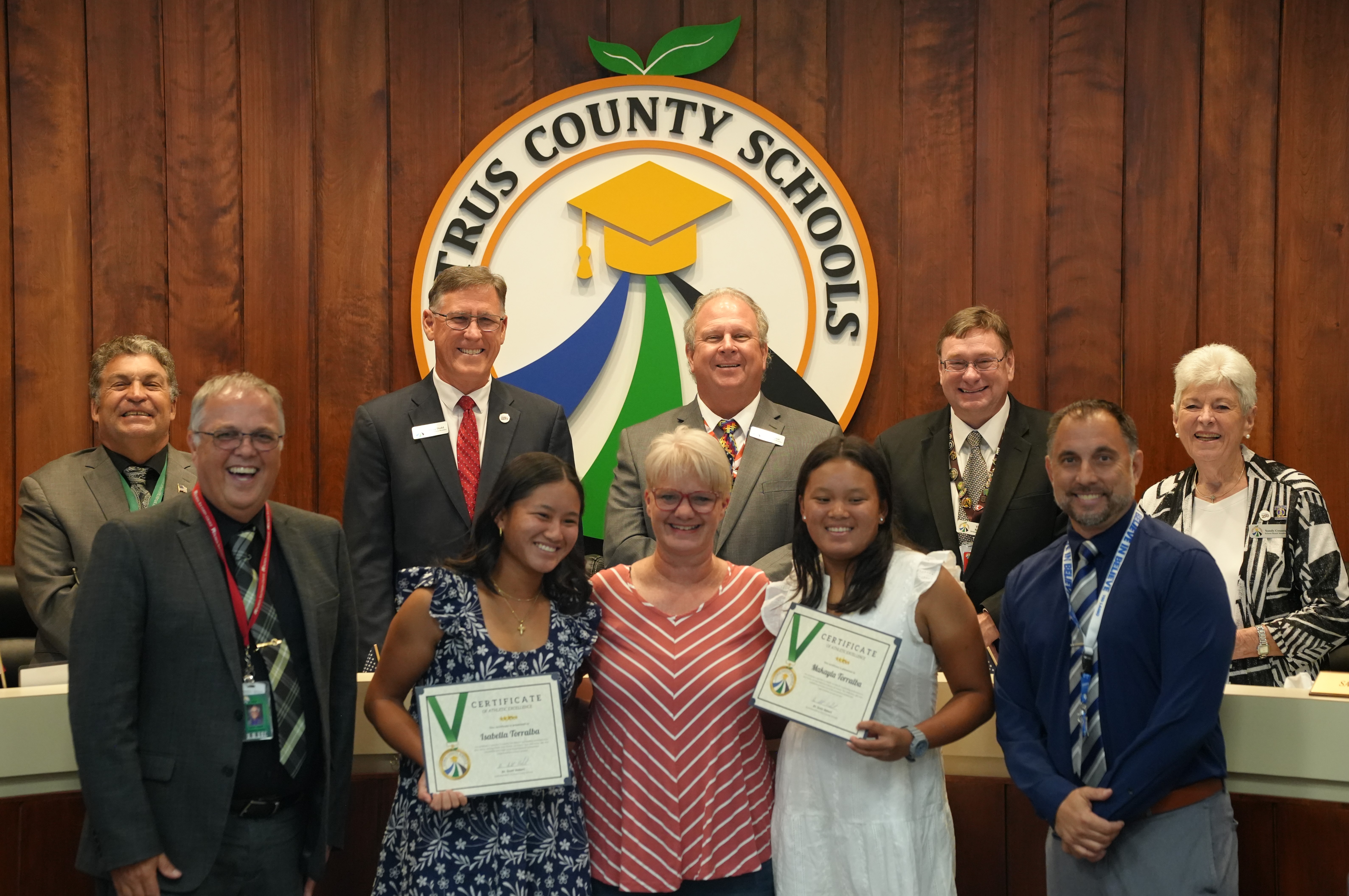 A group of adults and two young women smile for a photo in front of a Citrus County Schools logo.