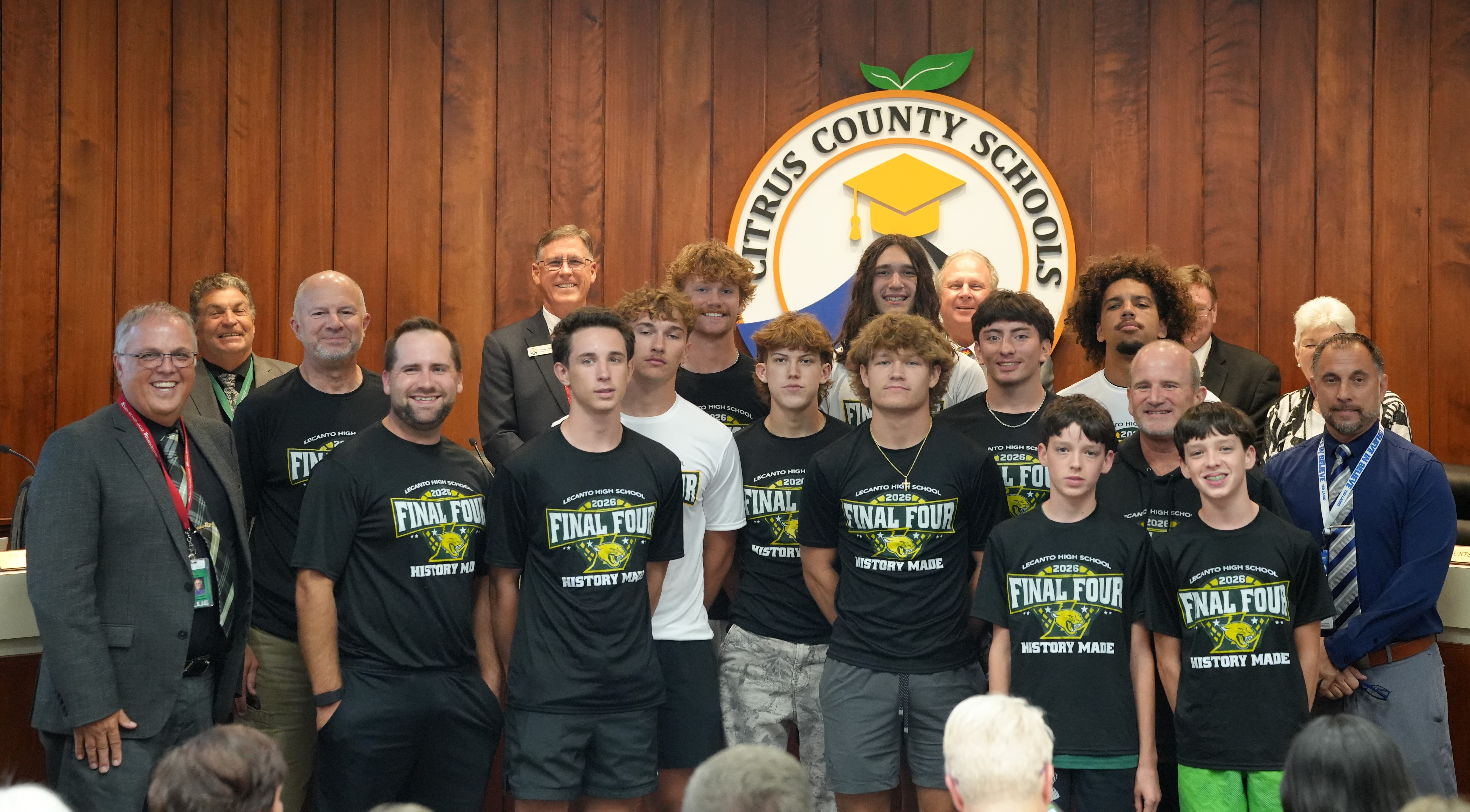 A group of students and adults pose for a photo in front of a wood-paneled wall with the Citrus County Schools logo.