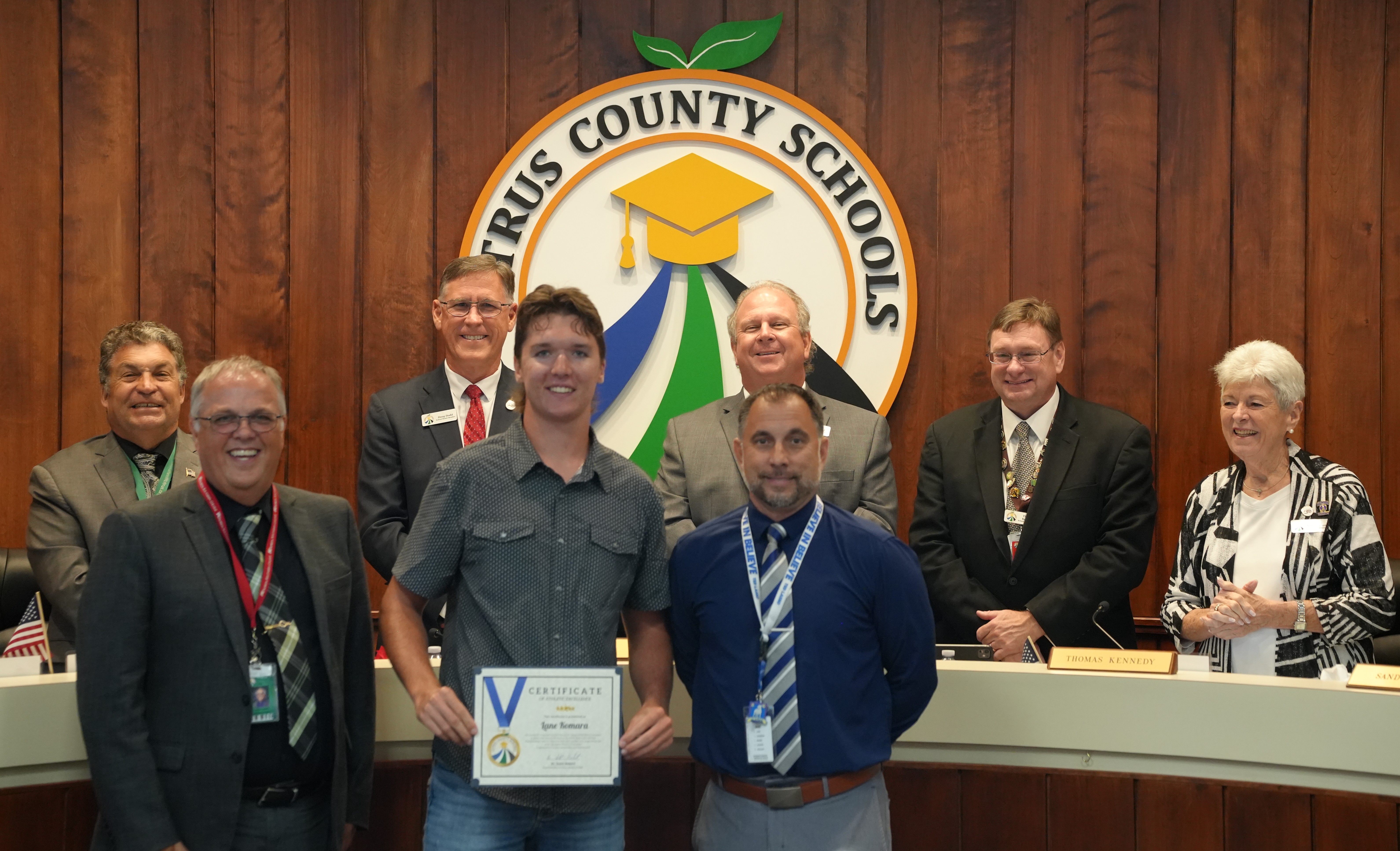 A group of people stand behind a podium with the Citrus County Schools logo, celebrating an award recipient.