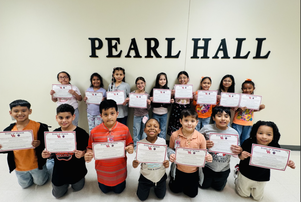 A group of elementary students proudly hold their certificates in front of a wall with the text "PEARL HALL".