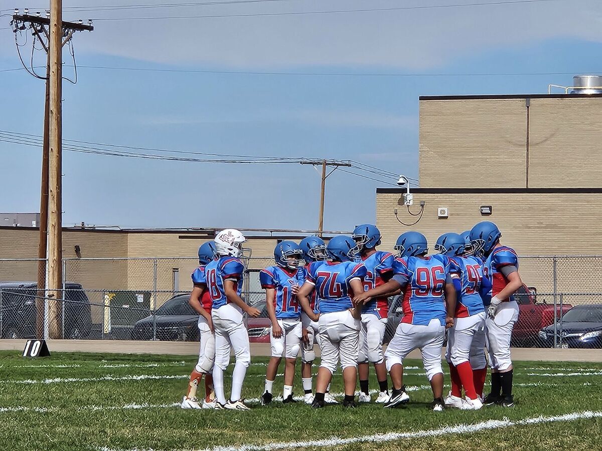 A youth football team in blue and red uniforms huddles together on a grassy field.