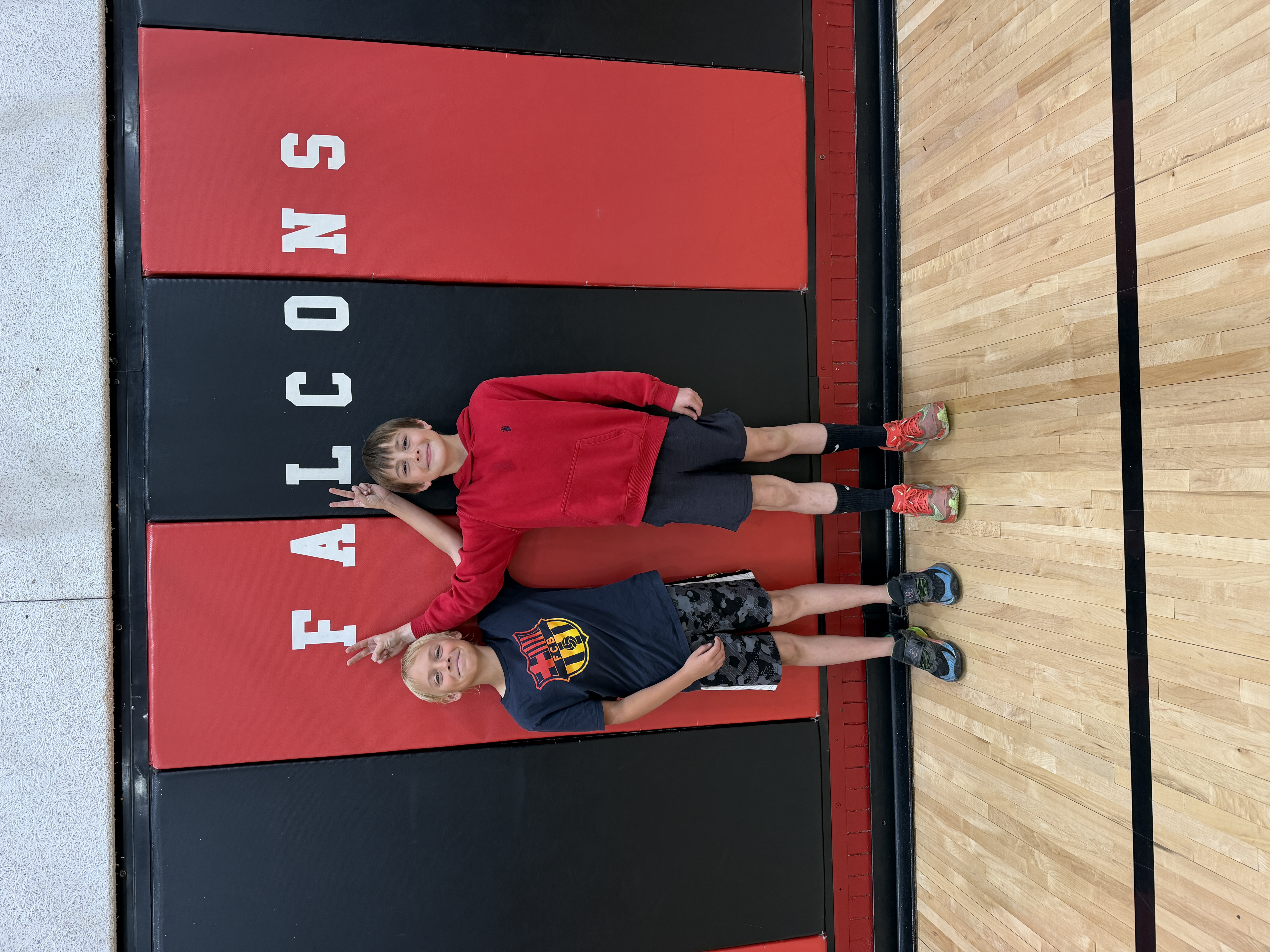 Two young boys lie on red and black mats with the word "FALCONS" visible.