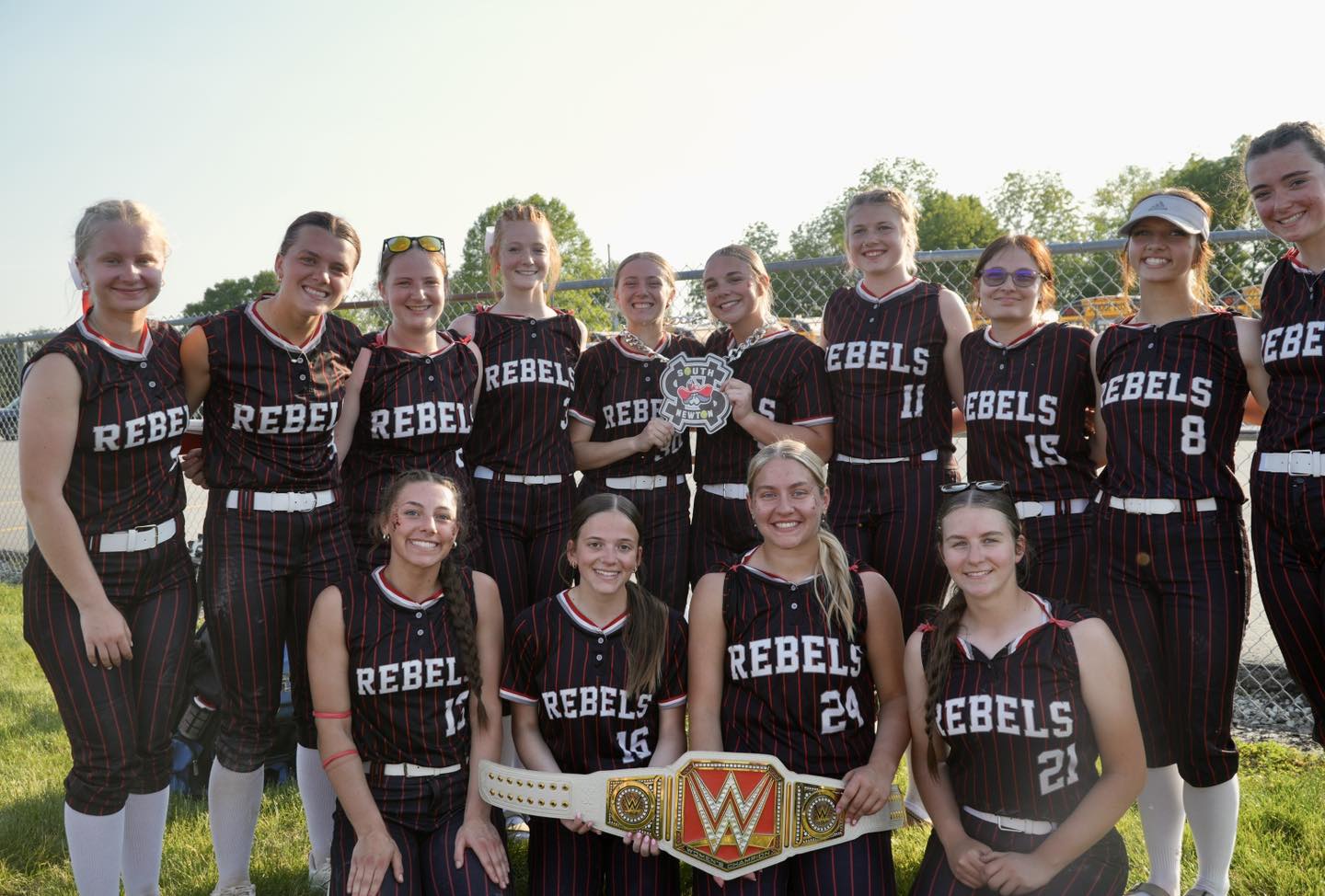A softball team, the Rebels, poses for a photo holding a championship belt and trophy.
