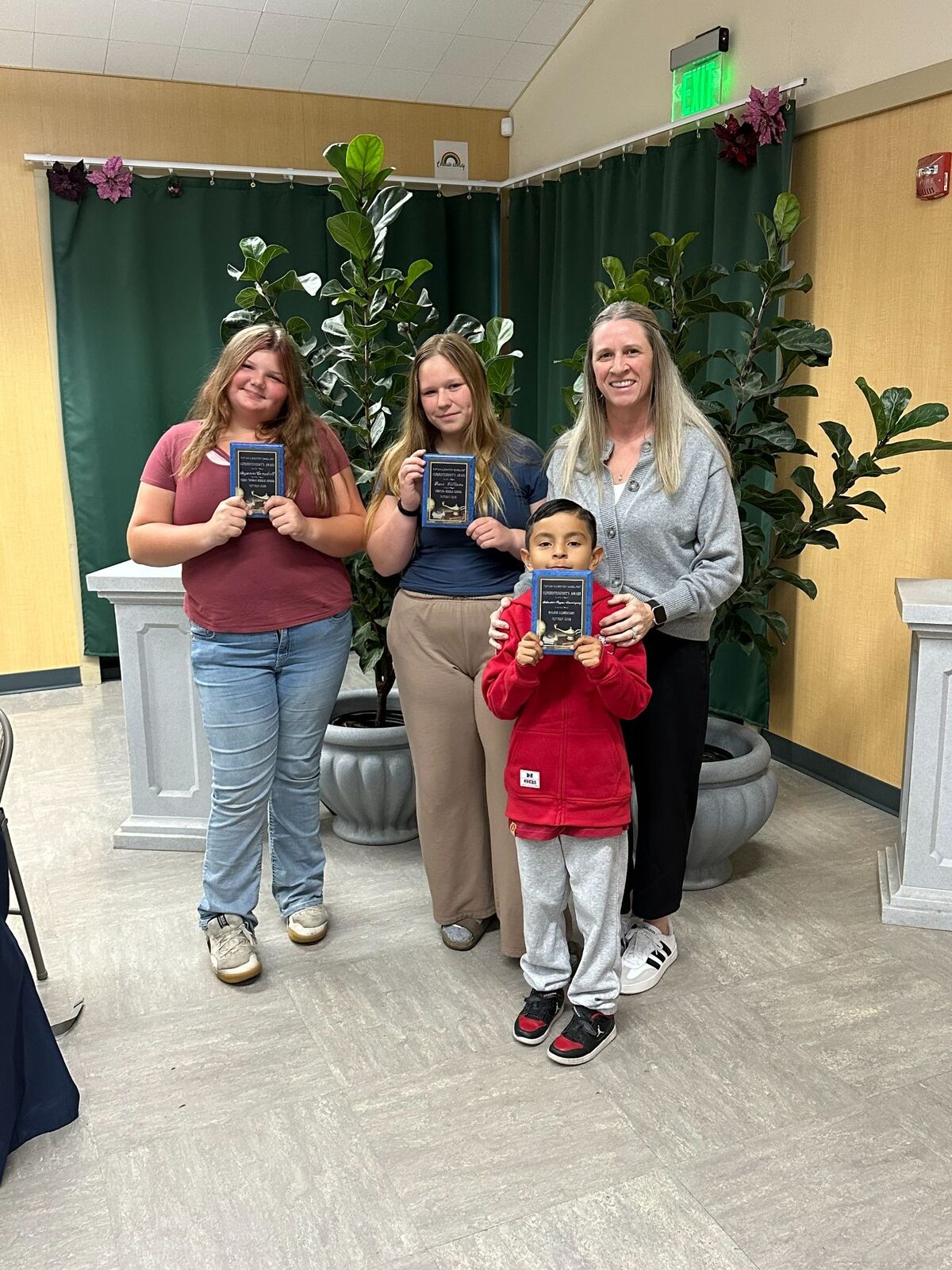 Three students and a woman proudly display their blue award plaques indoors.
