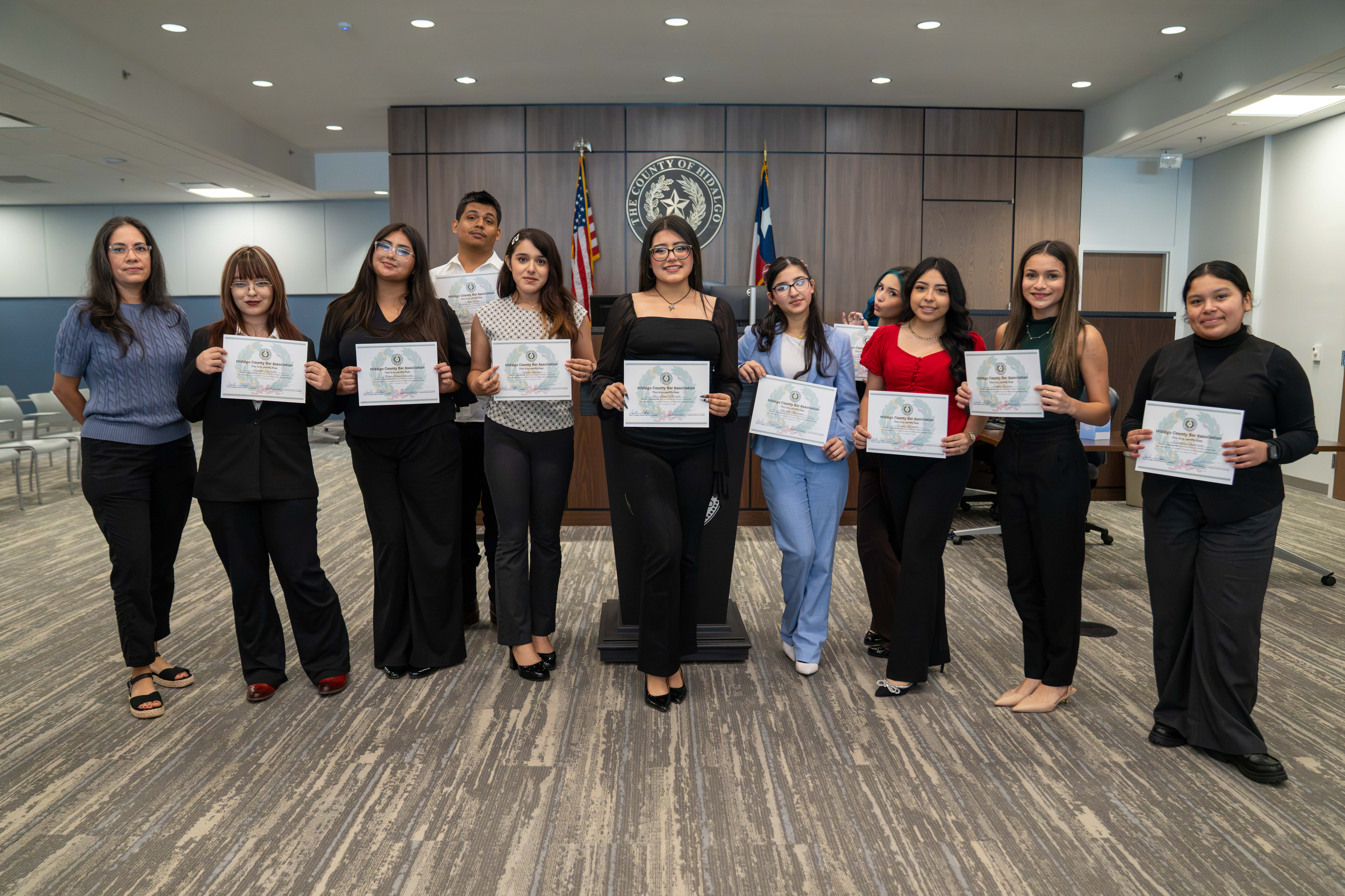 A group of young people stand proudly holding certificates in front of a "Hidalgo County" seal.