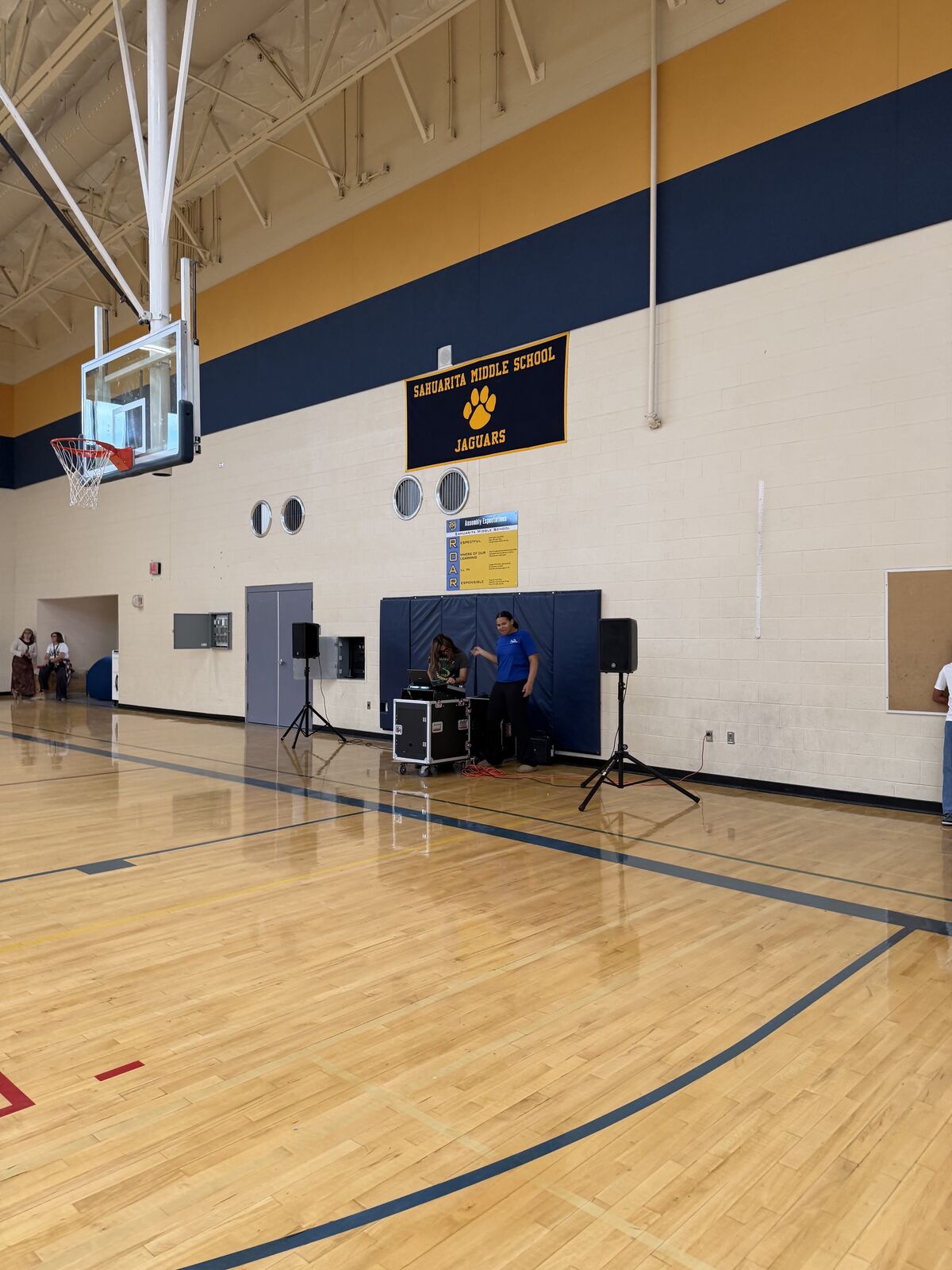 A basketball court with a banner for and two people setting up audio equipment.