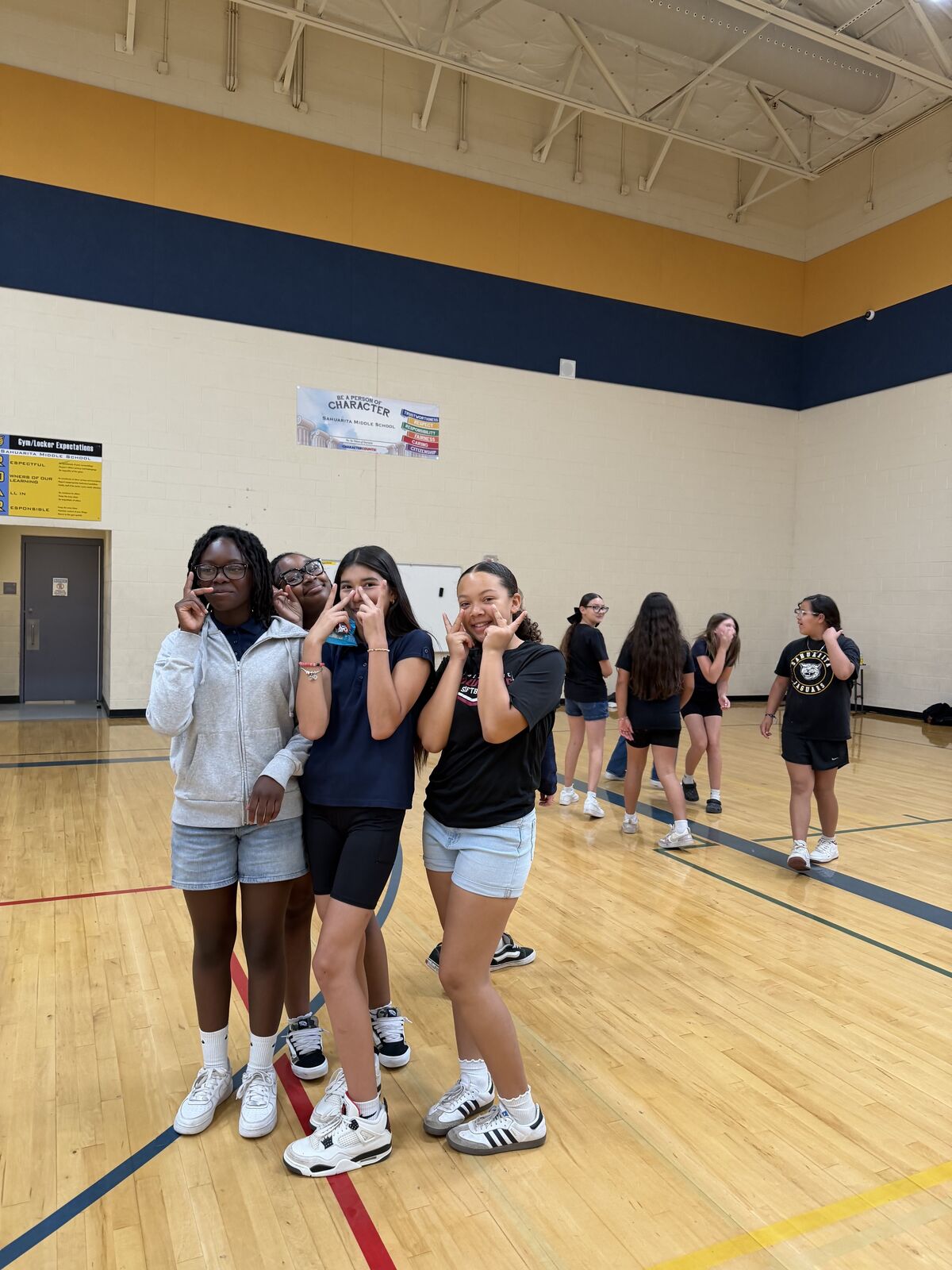 A group of young women in athletic wear pose for a photo on a wooden gym floor.