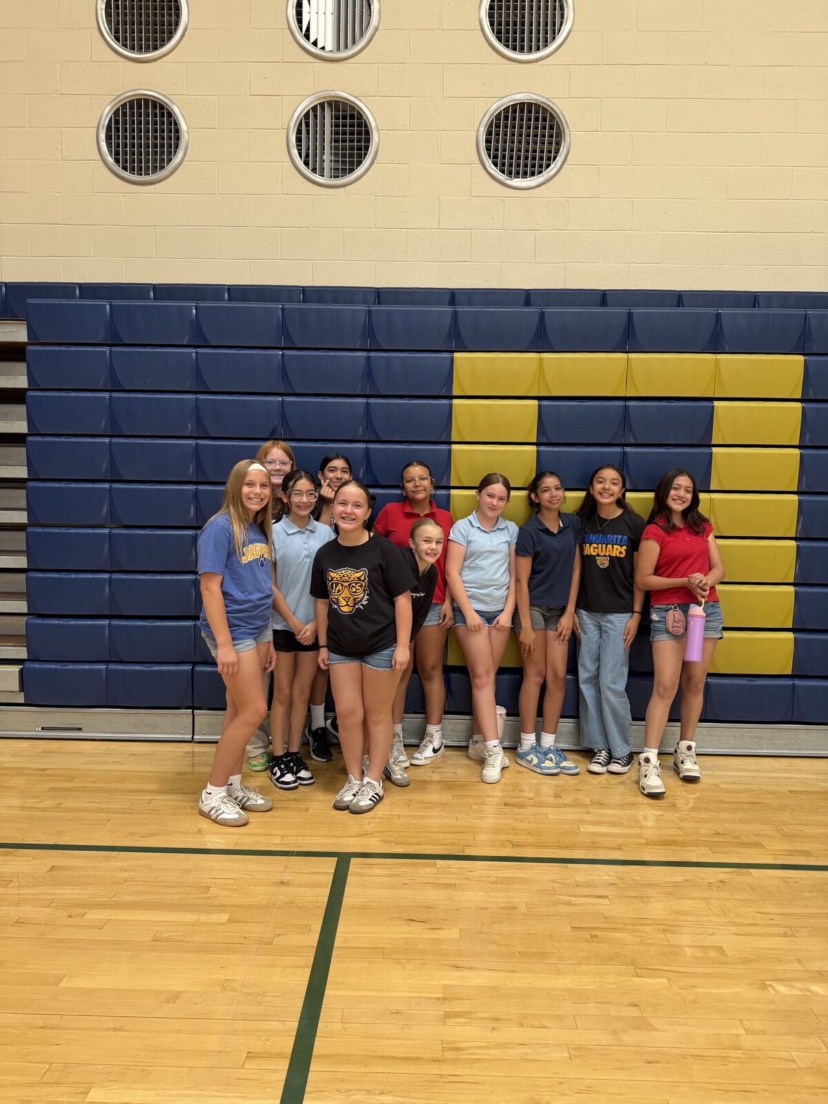 A group of smiling young women stand together in a gymnasium, posing for a photo.